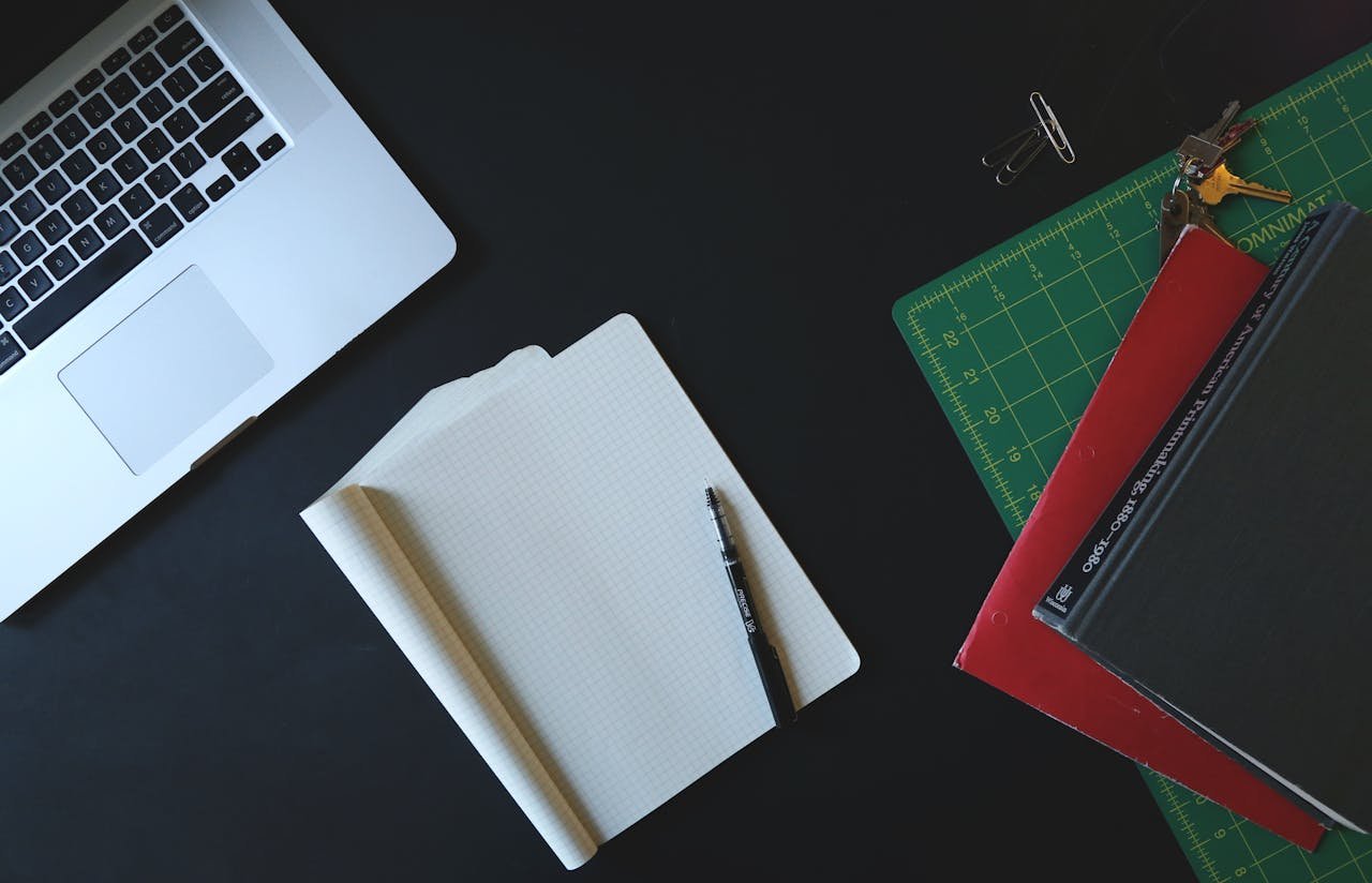 Top view of a modern workspace featuring a laptop, notebook, and office supplies on a black desk.